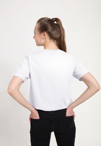 Hvid bomulds t-shirt med korte ærmer, rund hals og afslappet pasform, stylet med sorte jeans. Modellen står lidt drejet med hænderne i lommene.
