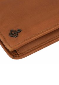 Braune Lederbörse mit sichtbaren Nähten, Faltendesign und einem metallischen Anker-Logo-Detail auf einer Seite. Glatte Textur mit leichtem Glanz.