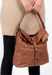 Sac en cuir marron avec une fermeture à rabat et une boucle en métal. Surface douce et texturée avec une seule poignée, porté au coude.