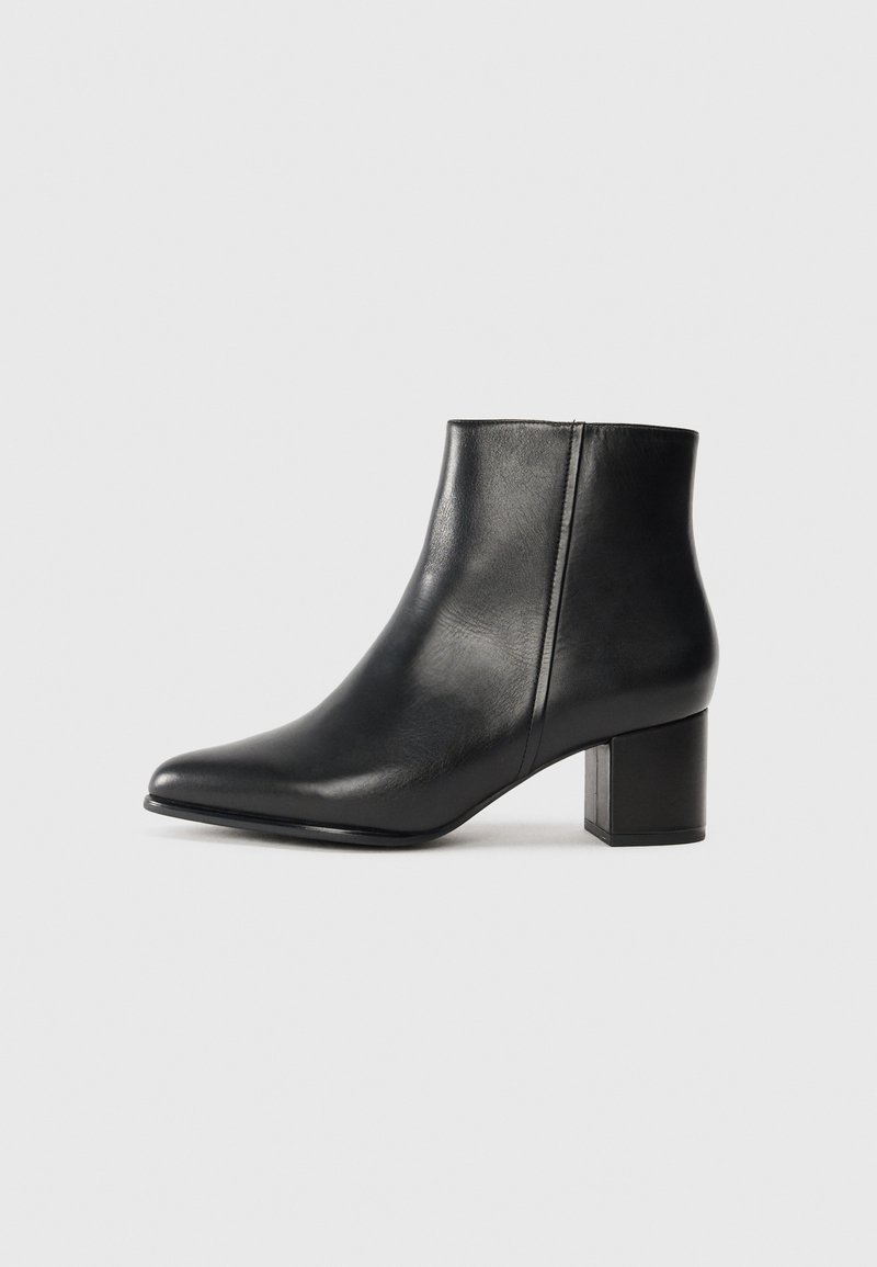 Botte de cheville en cuir noir avec un bout pointu et un talon bloc. Texture lisse et détails de couture minimalistes sur le dessus.