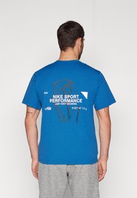 Camiseta de algodón azul con cuello redondo y mangas cortas. La parte posterior presenta el texto blanco "NIKE SPORT PERFORMANCE" y un diseño gráfico.