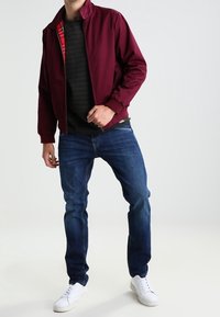Burgunderfarbene Bomberjacke mit Karofutter, schwarz gestreifter Pullover, blaue Jeans und weiße Sneaker. Lässiger Schnitt, glatte Textur und schlichtes Design.