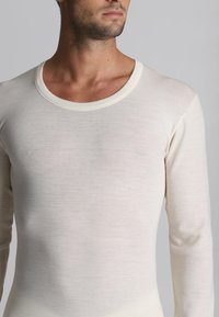 Camicia a maniche lunghe in cotone color crema, presenta una texture liscia e un ampio scollo rotondo. Design aderente evidenziato da maniche lunghe.