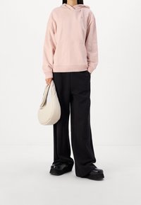 Felpa rosa chiaro con tasca frontale e orlo a costine, abbinata a pantaloni neri larghi. Il modello tiene una borsa color crema e indossa scarpe nere spesse.