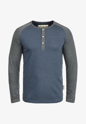 T-shirt à manches longues avec un corps bleu et des manches raglan grises. Il possède un col henley avec trois boutons et une étiquette sur le côté.