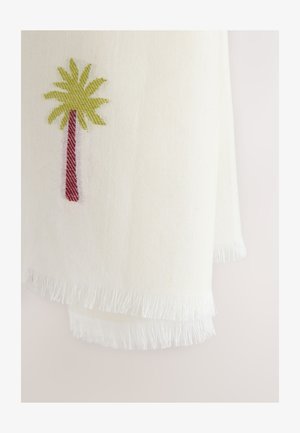 Hvid vævet stof med frynser i kanterne med et lille broderet palmetræ med brun stamme og grønne blade.