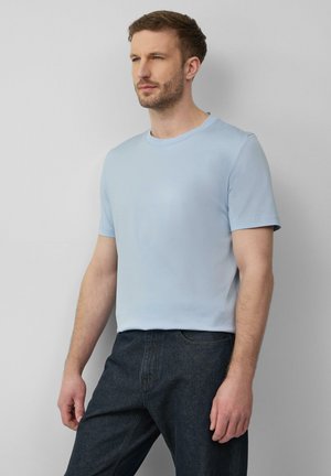 Helltürkises T-Shirt mit kurzen Ärmeln, aus weichem Stoff, mit Rundhalsausschnitt und lockerer Passform. Kombiniert mit dunklen Jeans.