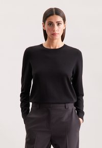 Czarny sweter z długim rękawem i okrągłym dekoltem, wykonany z miękkiego materiału, w połączeniu z dopasowanymi ciemnymi spodniami. Prosty, teksturowany design.