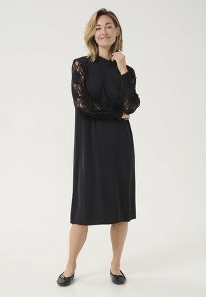 Black dress with lace sleeves and a high neckline. The fabric is smooth, and the shape is relaxed, falling just above the knee.