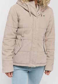 Beżowa kurtka puchowa z kapturem z kordurowej tkaniny, z pikowanym wypełnieniem, bocznymi kieszeniami i zapięciem na suwak z przodu. Miękka, strukturalna tkanina.