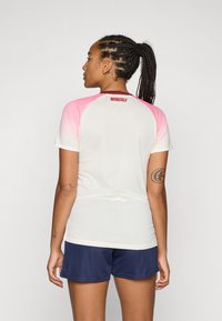 Sport shirt with short sleeves, white body, pink gradient sleeves, and logo on the back. Paired with dark blue athletic shorts.