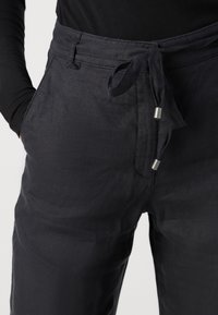 Svarta linnebyxor med knytbar midja och metalliska detaljer, med en smidig textur och minimalistisk design, visade från midjan och ner.