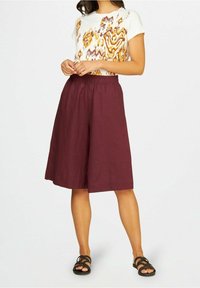 Burgundské lněné culoty s elastickým pasem, v kombinaci s bílou košilí s krátkým rukávem, která má barevný květinový vzor. Černé sandály.