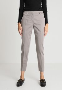 Světle šedé zakázkově šité kalhoty se slim fit střihem, které mají přední kapsy a plochý přední design. Kombinované s černým topem s dlouhým rukávem a mokasíny.