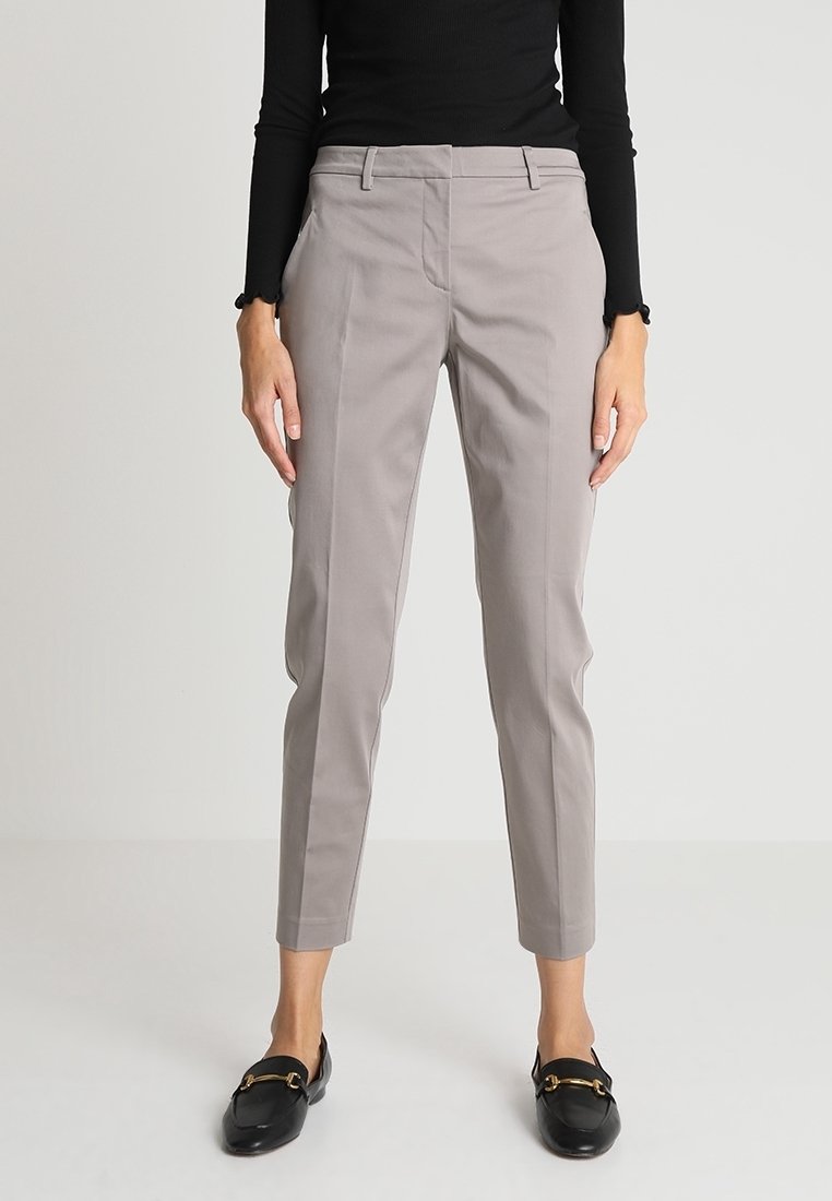 Světle šedé zakázkově šité kalhoty se slim fit střihem, které mají přední kapsy a plochý přední design. Kombinované s černým topem s dlouhým rukávem a mokasíny.