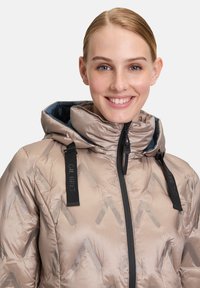 Licht beige pufferjack met een capuchon, voorzien van een geometrisch patroon, zwarte ritsen en merkbanden. Gladde textuur, geïsoleerd ontwerp.