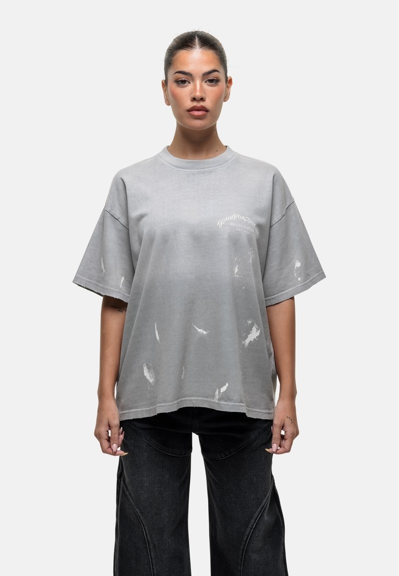 Szara, oversize koszulka z wystrzępionymi detalami i okrągłym dekoltem. Posiada drukowany tekst w kolorze białym. Materiał ma miękki, znoszony wygląd.