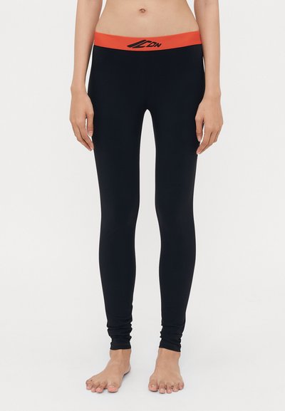 Schwarze Leggings mit enger Passform, ausgestattet mit einem breiten roten Elastikbund mit einem Logo. Glatte Textur, Knöchellänge.