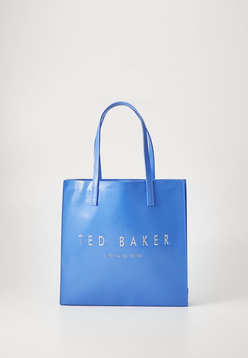 Plava torba od umjetne kože s dugim ručkama i srebrnim logotipom "TED BAKER LONDON" na prednjoj strani. Glatka tekstura, pravokutni oblik.