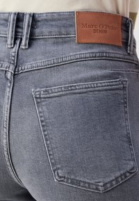 Grå denimjeans med en läderetikett präglad med "Marc O'Polo DENIM." Inkluderar synlig sömnad och en detalj på bakfickan.