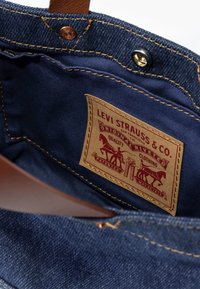 Μπλε τζιν εσωτερικό ενός προϊόντος της Levi Strauss & Co. που διαθέτει ραμμένη δερμάτινη ετικέτα με κόκκινες γραφικές παραστάσεις και χρυσές λεπτομέρειες.
