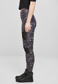 Svart leggings med et hvitt himmelmønster og mesh-paneler, med en tettsittende design og utskjæringer på hoftene. Parret med høyhælte svarte joggesko.