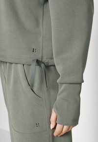Conjunto de joggers elásticos en tela verde suave, con cintura ajustable con cordón, bolsillos laterales y puños acanalados con un detalle de logotipo sutil.