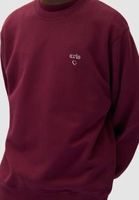 Felpa bordeaux realizzata in morbido tessuto, con scollatura rotonda e logo ricamato bianco con design a cuore sul petto.