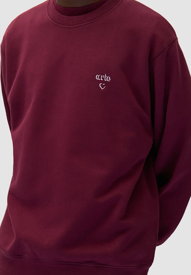 Felpa bordeaux realizzata in morbido tessuto, con scollatura rotonda e logo ricamato bianco con design a cuore sul petto.