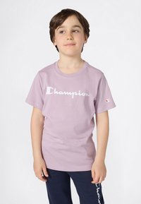 Camiseta de algodón lila con el logotipo blanco de "Champion" en el frontal, con mangas cortas y escote redondo.