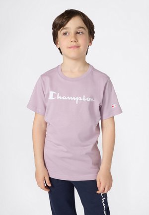 T-shirt en coton lilas avec un logo "Champion" blanc sur le devant, à manches courtes et col rond.