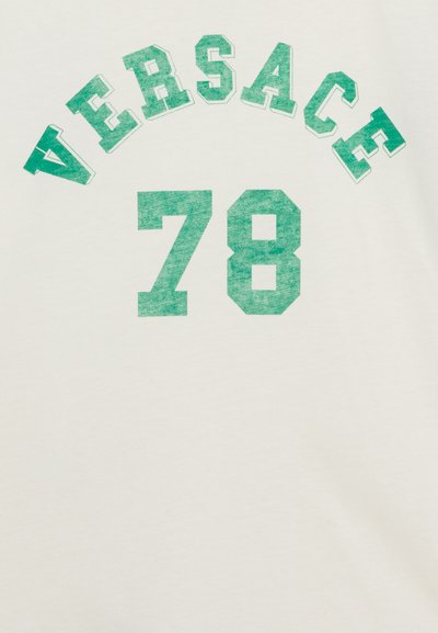 Valge puuvillane T-särk, millel on suured rohelised plokktähed, mis ütlevad "VERSACE" kaares ja number "78" keskel all, vanutatud tekstuuriga.