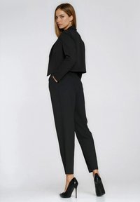 Czarny krótki blezer o dopasowanym kroju, zestawiony z dopasowanymi czarnymi spodniami. Oba elementy mają gładką strukturę i czyste linie.