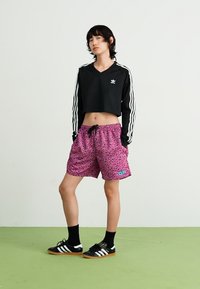 Sweatshirt preto encurtado com riscas brancas, combinado com calções cor-de-rosa com padrão de leopardo. Modelo usa meias e sapatos pretos com riscas.