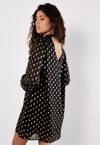 Schwarzes Kleid mit goldenen Punktemuster, leichtem V-Ausschnitt auf der Rückseite, langen Puffärmeln, leichtem Stoff, lockerer Passform, knielang und weicher Textur.