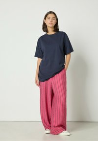 Mornarsko plava oversized majica s teksturiranim dizajnom, u kombinaciji s opuštenim ružičastim hlačama na pruge koje imaju bijele vertikalne linije i bijelim tenisicama.