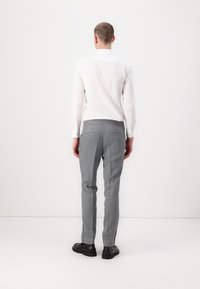 Graue, maßgeschneiderte Hose mit glatter Textur, seitlichen Schlitzen und schlanker Passform, kombiniert mit einem weißen Hemd mit Knopfleiste, von hinten betrachtet.
