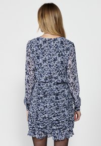 Kukallinen mekko sinisen ja laventelin sävyissä, rypytetyllä muotoilulla, pitkät hihat ja röyhelöhelma. Hienot kankaat hihoissa.