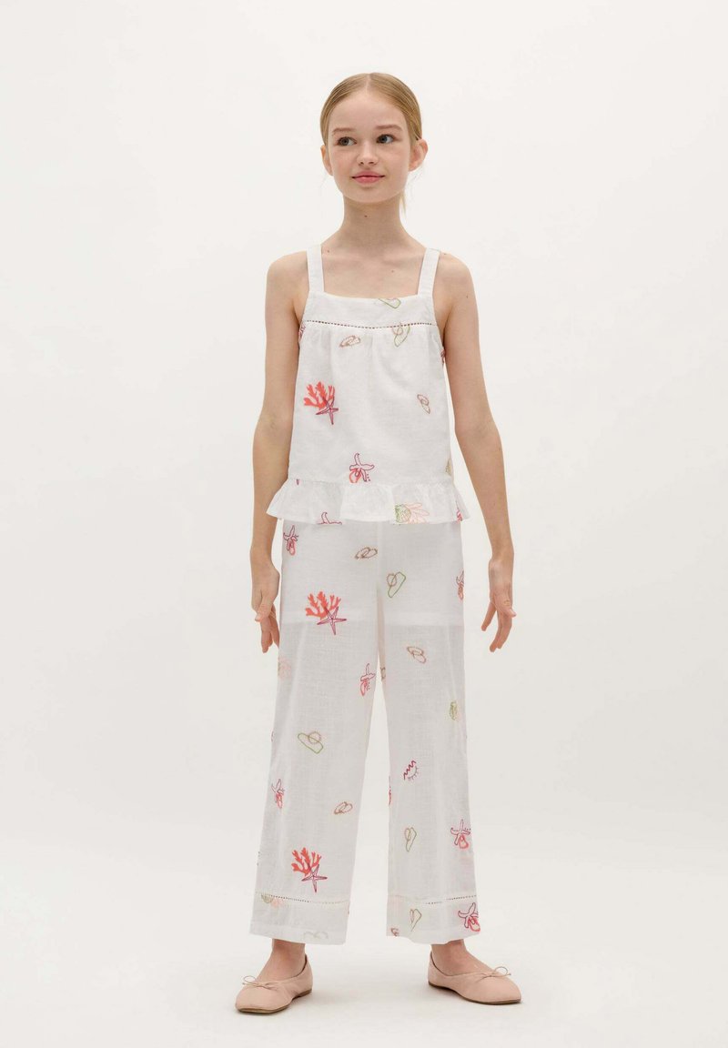 Weißes ärmelloses Top mit bestickten Korallen- und Blättermustern, kombiniert mit locker sitzenden weißen Hosen mit ähnlichen Designs. Glatte Textur.