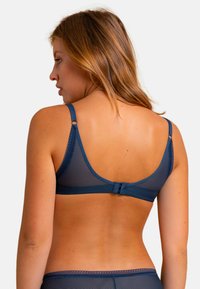 Soutien-gorge en maille bleu marine avec bretelles réglables, bordure en dentelle et fermeture à crochets. Présente une texture lisse et semi-transparente ainsi que des bords arrondis.