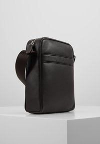 Borsa a tracolla nera in pelle, dalla forma rettangolare, superficie texture, chiusura con zip e tracolla removibile. Presenta un dettaglio con tasca frontale.