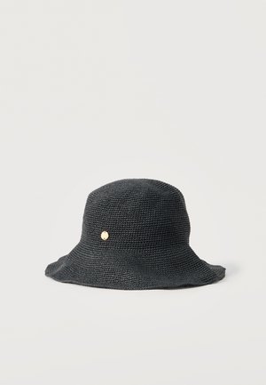 Schwarzer gestrickter Anglerhut mit breiter, lockerer Krempe und kleinem rundem goldfarbenem Emblem an der Seite, vor einem schlichten hellen Hintergrund.