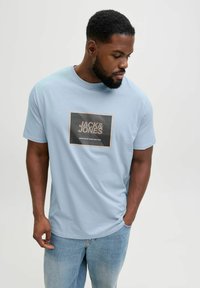 Lyseblå bomuld T-shirt med korte ærmer, der har et rektangulært grafisk logo i sort og hvid med orange accenter på forsiden.