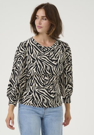 Zwart en beige shirt met zebra-stripes, voorzien van een ronde halslijn en pofmouwen, gemaakt van gestructureerde stof. Gecombineerd met lichtblauwe jeans.