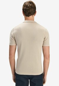 Beige ribbad polo paita lyhyillä hihoilla, jossa on kaulus ja hienovarainen pinta. Istuvuus on napakka, korostaen vartalon muotoa.