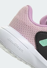 Tige en mesh rose avec une semelle en caoutchouc, comportant un accent noir et un détail de design couleur menthe. Surface texturée et tissu respirant.