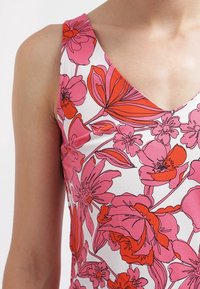 Halenka s květinovým potiskem s živými růžovými a oranžovými květy na bílém pozadí, s hlubokým výstřihem do V a přiléhavým střihem.