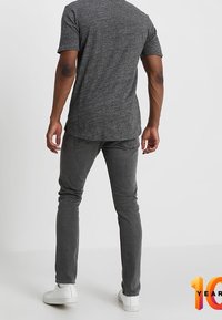 Camisa gris de manga corta y jeans ajustados gris oscuro. El atuendo se complementa con zapatillas blancas. Diseño simple y casual sin patrones ni acentos.