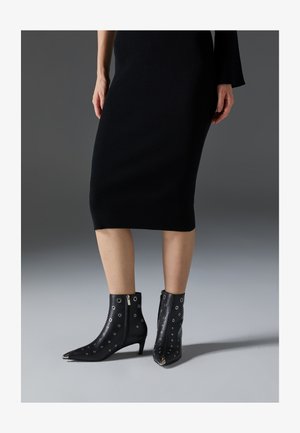 Schwarze Leder-Stiefeletten mit spitzer Zehenform, die runde Aussparungen und Seitenreißverschlüsse aufweisen. Der Absatz ist moderat und strukturiert.