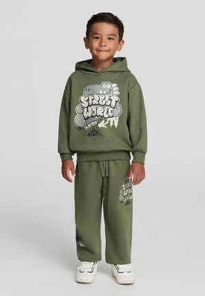 Felpa verde oliva con grafica "STREET WORLD" e pantaloni abbinati con design simile. Materiale in cotone e vestibilità rilassata.